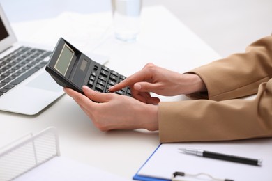 Woman using calculator at table indoors, closeup