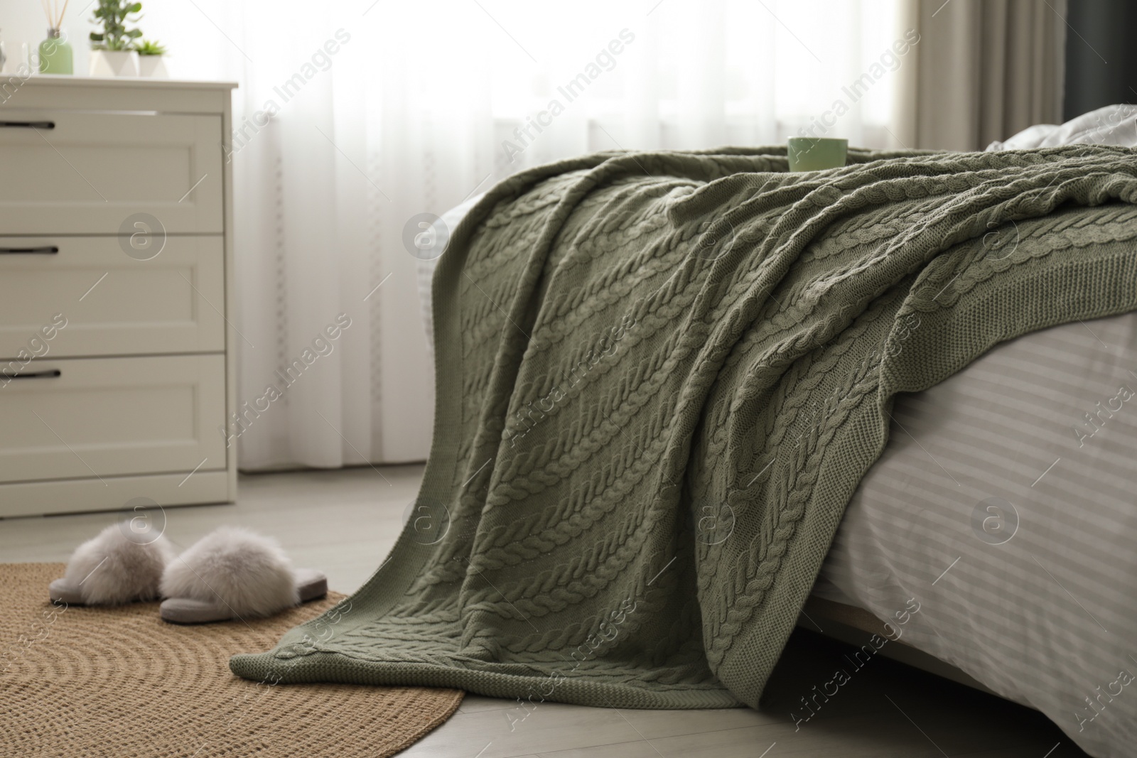 Photo of Comfortable bed with knitted green plaid in stylish room interior