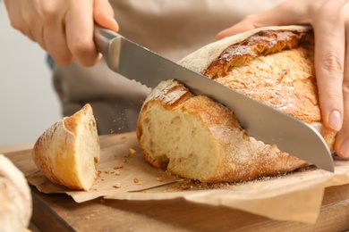 Woman cutting freshly baked bread at wooden table, closeup