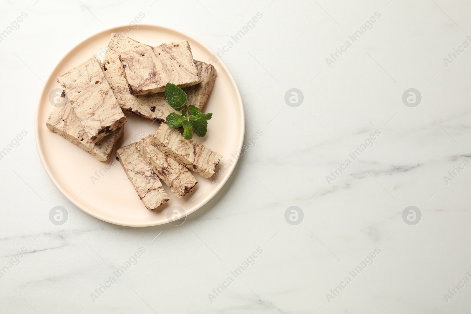 Photo of Pieces of tasty chocolate halva and mint on white marble table, top view. Space for text