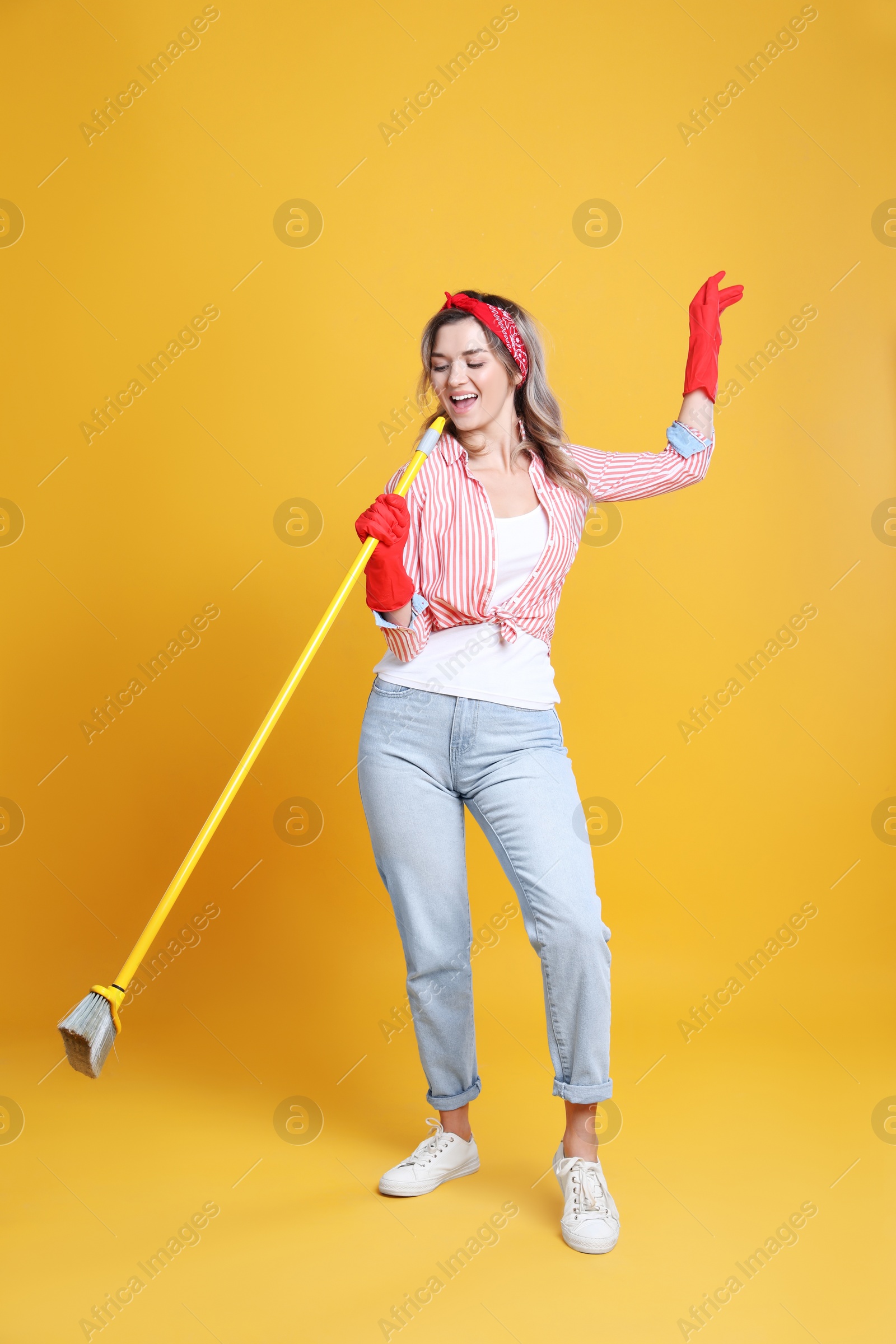 Photo of Beautiful young woman with floor brush singing on orange background