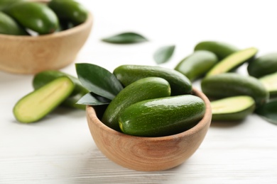 Photo of Fresh seedless avocados with green leaves in bowl on white wooden table, closeup