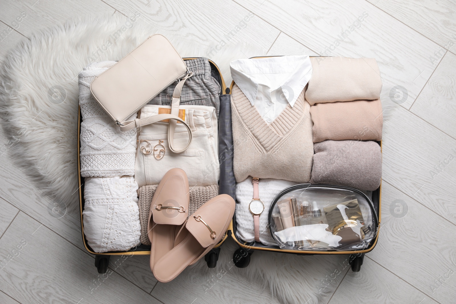 Photo of Open suitcase with folded clothes, shoes and accessories on floor, top view