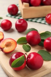 Photo of Delicious ripe cherry plums with leaves on white wooden table