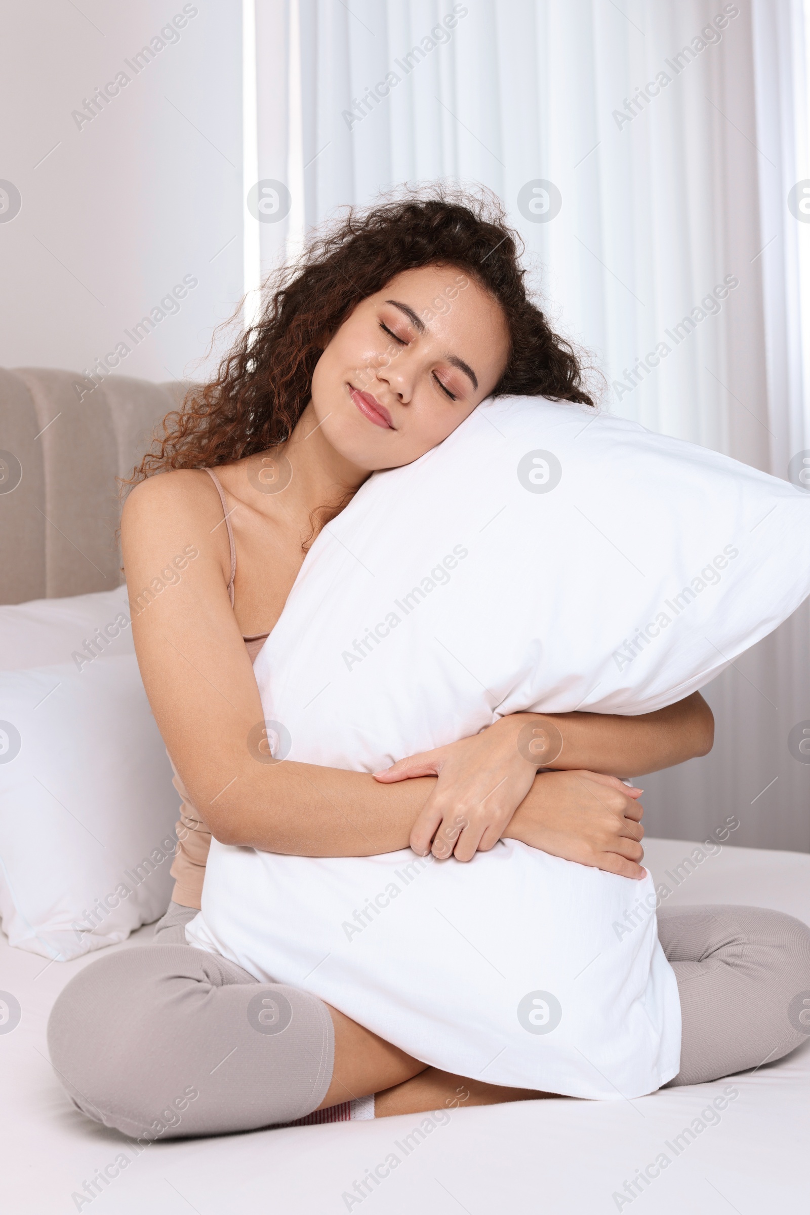 Photo of Happy African American woman hugging soft pillow on bed at home