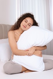 Photo of Happy African American woman hugging soft pillow on bed at home