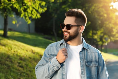 Handsome smiling man wearing sunglasses in park, space for text