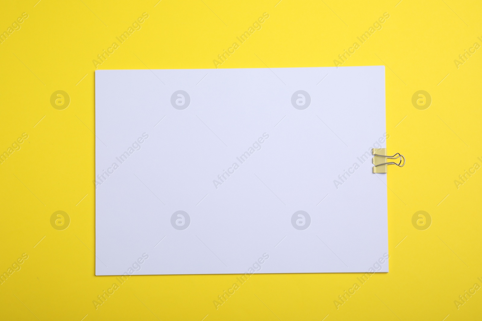 Photo of Sheet of paper with clip on yellow background, top view