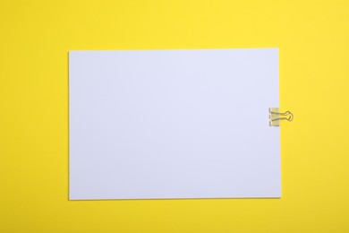 Photo of Sheet of paper with clip on yellow background, top view