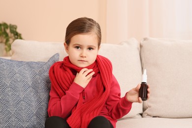 Photo of Cute little girl holding nasal spray on sofa at home