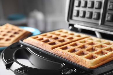 Modern iron with tasty Belgian waffles on table, closeup