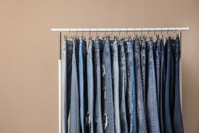 Photo of Rack with stylish jeans on beige background