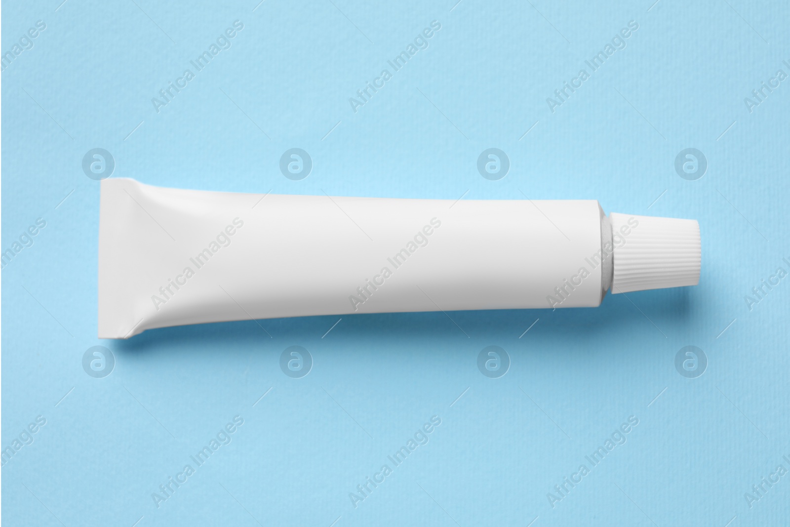 Photo of Tube of ointment on light blue background, top view. Space for text