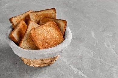 Photo of Wicker basket with slices of delicious toasted bread on gray marble table
