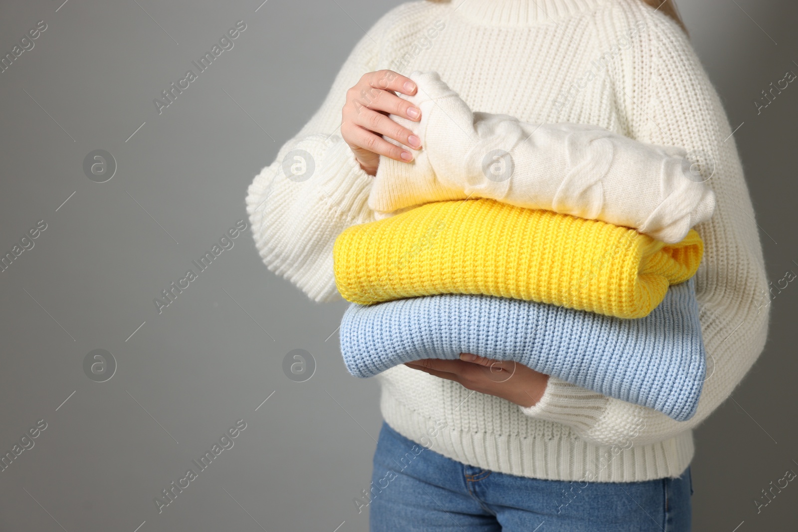 Photo of Woman with stack of knitted sweaters on grey background, closeup. Space for text