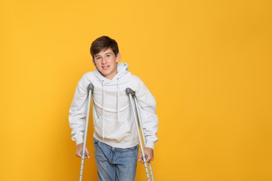 Photo of Teenage boy with injured leg using crutches on yellow background, space for text