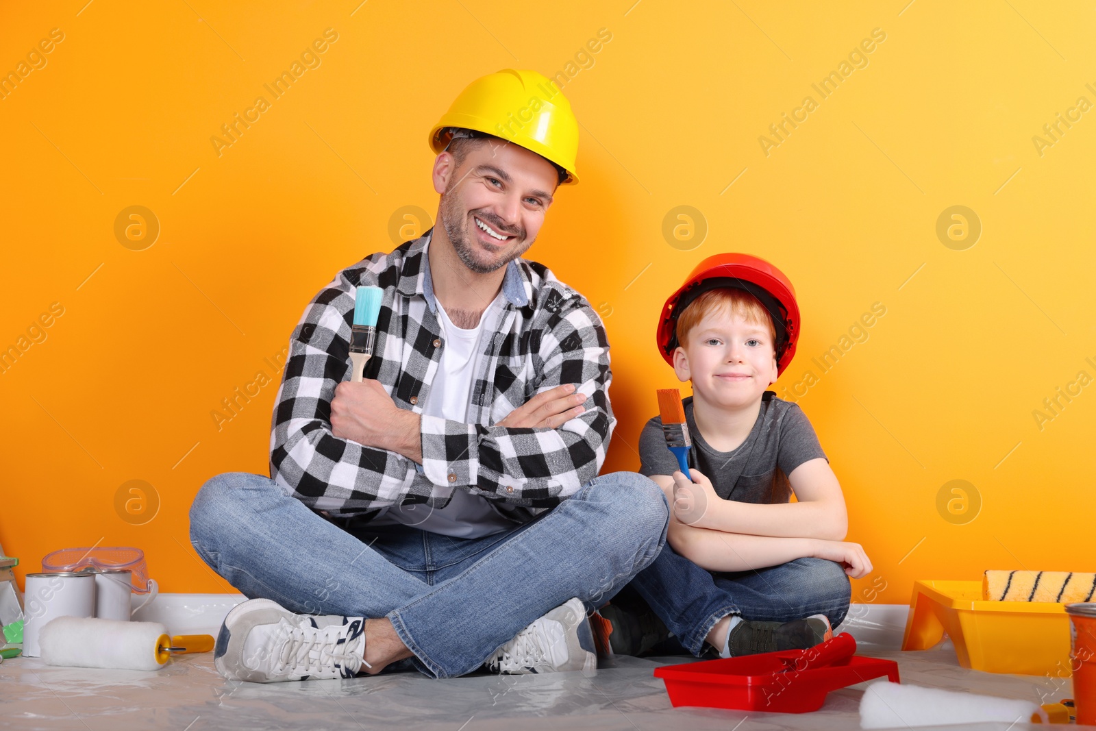 Photo of Father and son with repair tools near orange wall