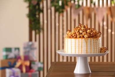 Photo of Caramel drip cake decorated with popcorn and pretzels on wooden table, space for text