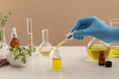 Scientist with cosmetic oil at white table, closeup