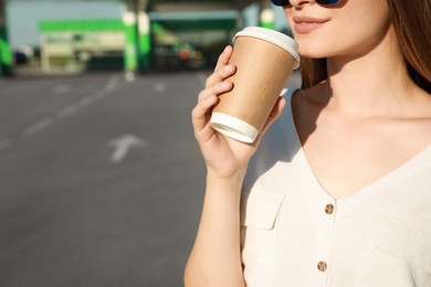 Photo of Beautiful young woman drinking coffee at gas station, closeup. Space for text