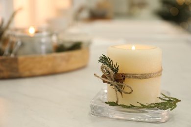Photo of Burning scented conifer candle on white table indoors. Space for text