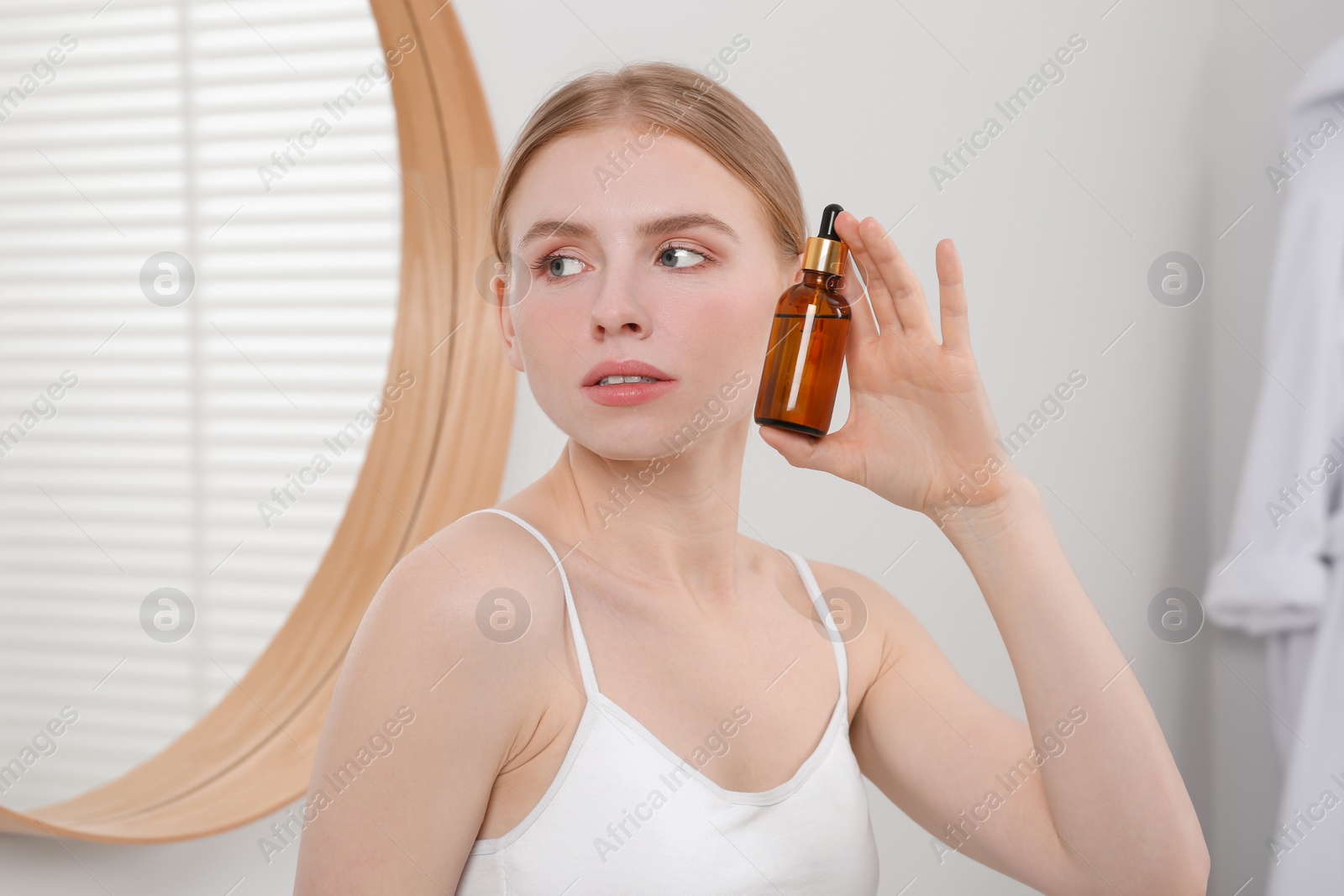 Photo of Young woman with bottle of essential oil in bathroom