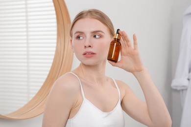 Young woman with bottle of essential oil in bathroom