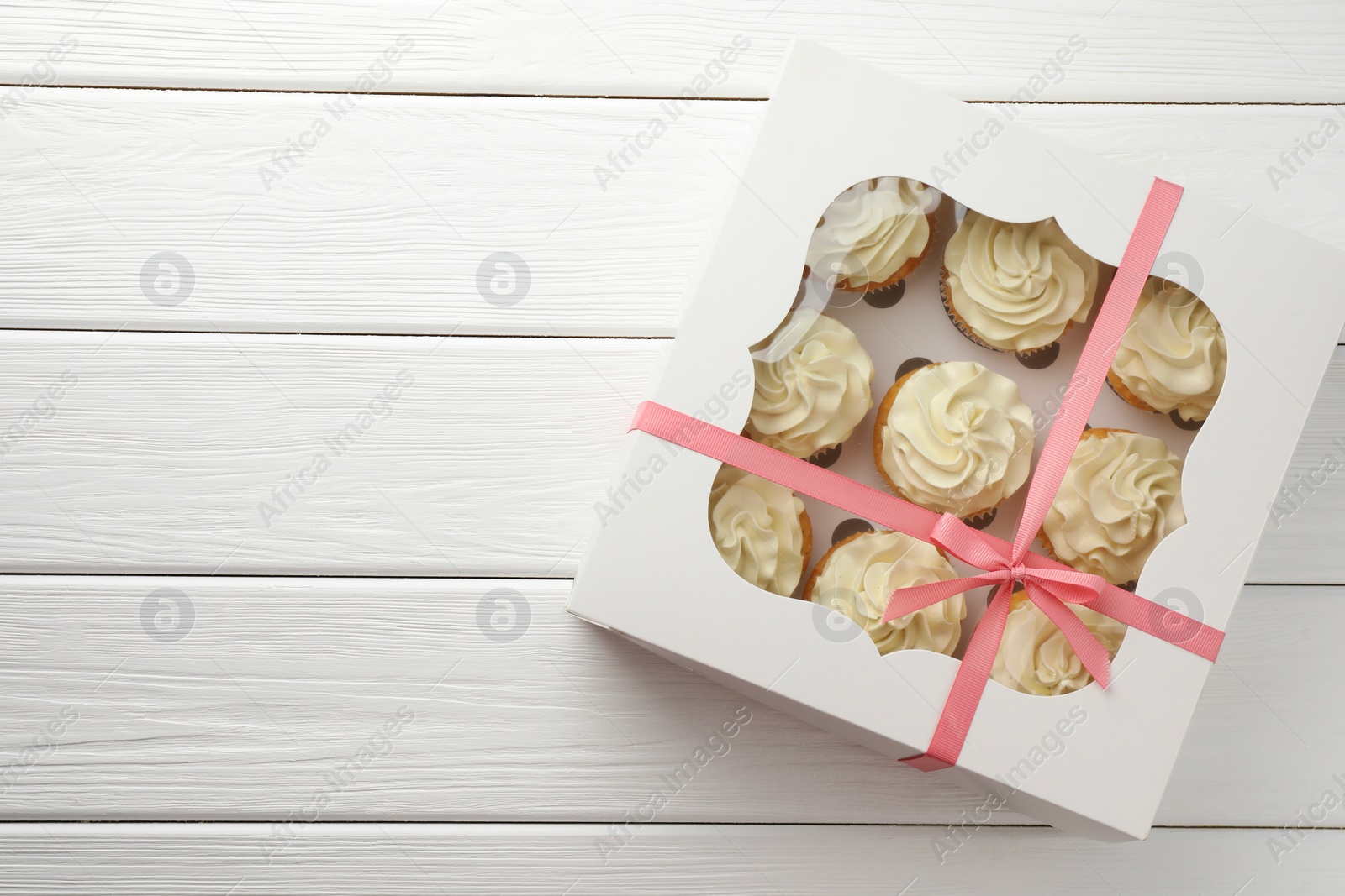 Photo of Tasty cupcakes with vanilla cream in box on white wooden table, top view. Space for text