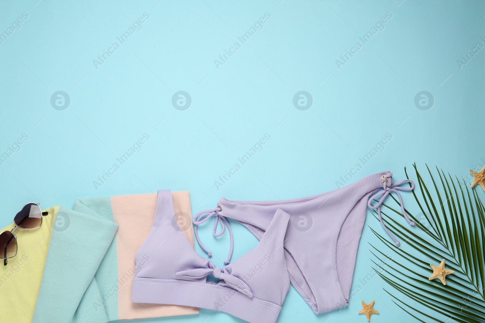 Photo of Beach towel, swimsuit and sunglasses on light blue background, flat lay. Space for text