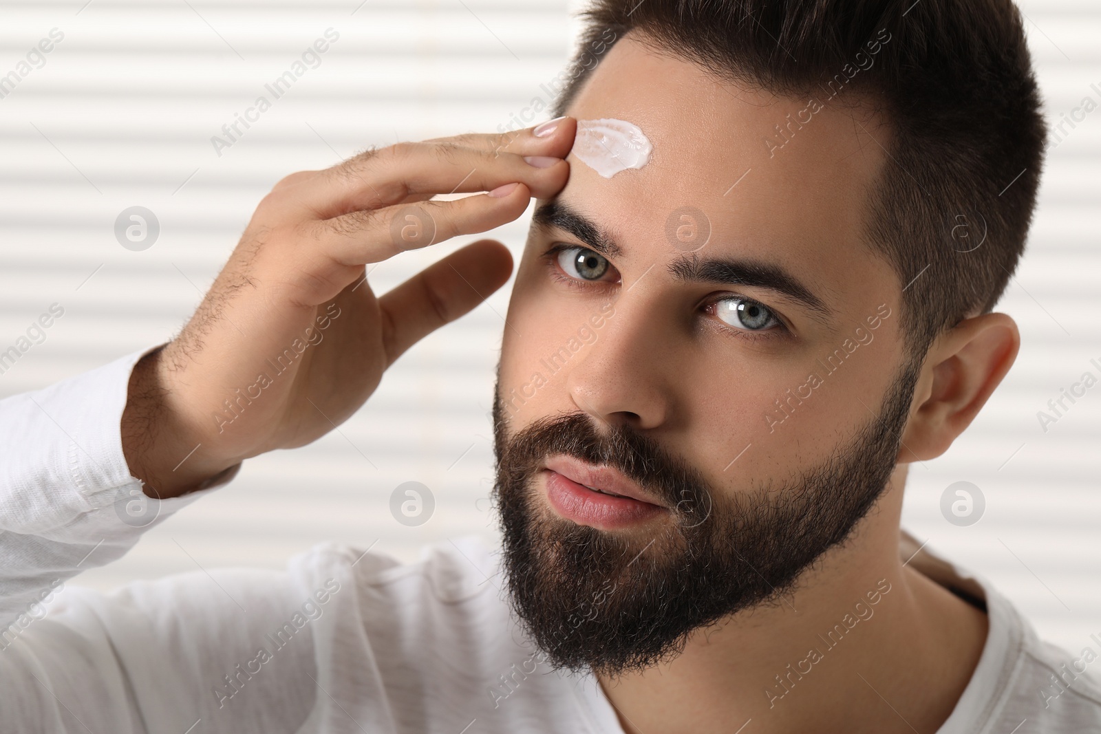 Photo of Man with dry skin applying cream onto his forehead indoors