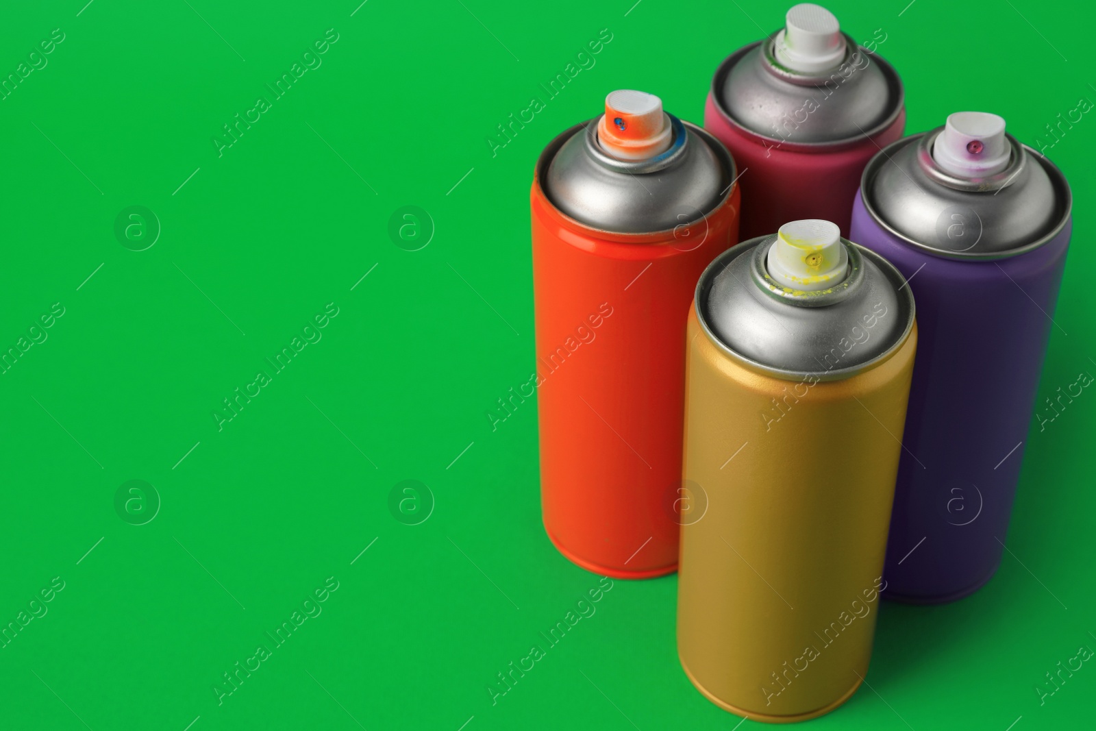 Photo of Cans of different graffiti spray paints on green background, space for text