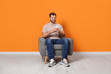 Photo of Young man using smartphone while sitting in armchair indoors