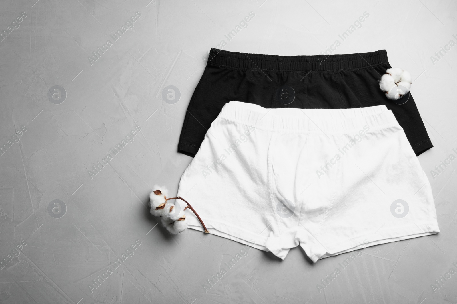 Photo of Comfortable men's underwear and cotton flowers on light grey stone background, flat lay