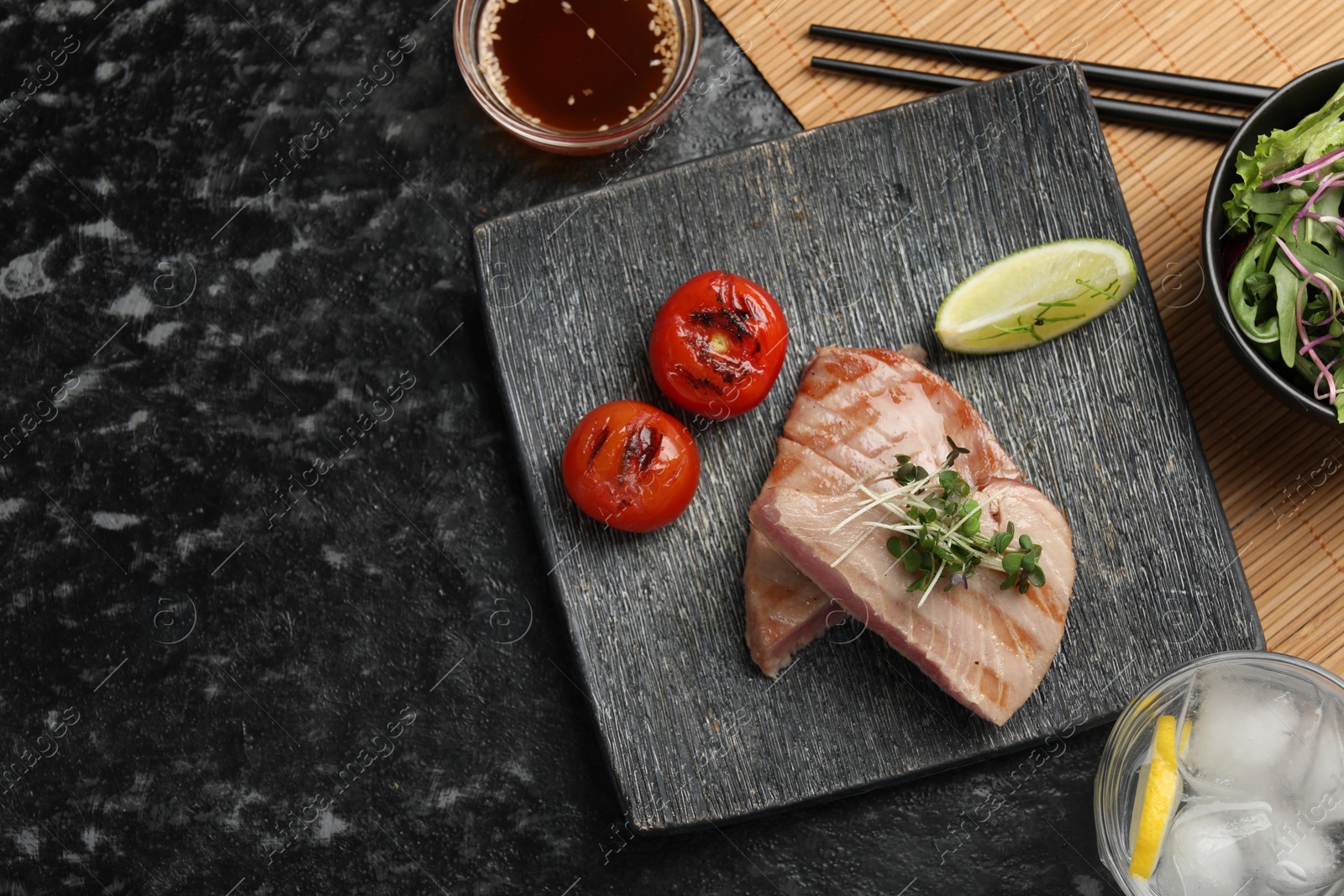 Photo of Pieces of delicious tuna with lime and tomatoes served on black table, flat lay. Space for text