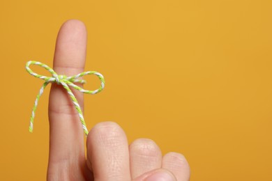 Woman showing index finger with tied bow as reminder on orange background, closeup. Space for text