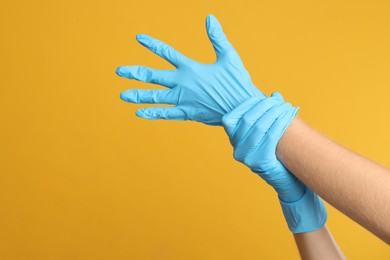 Doctor wearing medical gloves on yellow background, closeup. Space for text