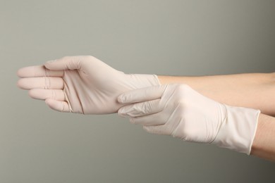 Person putting on medical gloves against grey background, closeup of hands