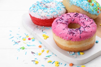 Photo of Sweet glazed donuts decorated with sprinkles on white wooden table, space for text. Tasty confectionery