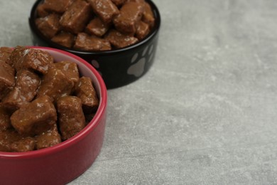 Photo of Wet pet food in feeding bowls on light grey background. Space for text