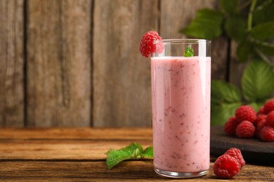 Glass of tasty fresh raspberry smoothie on wooden table, space for text