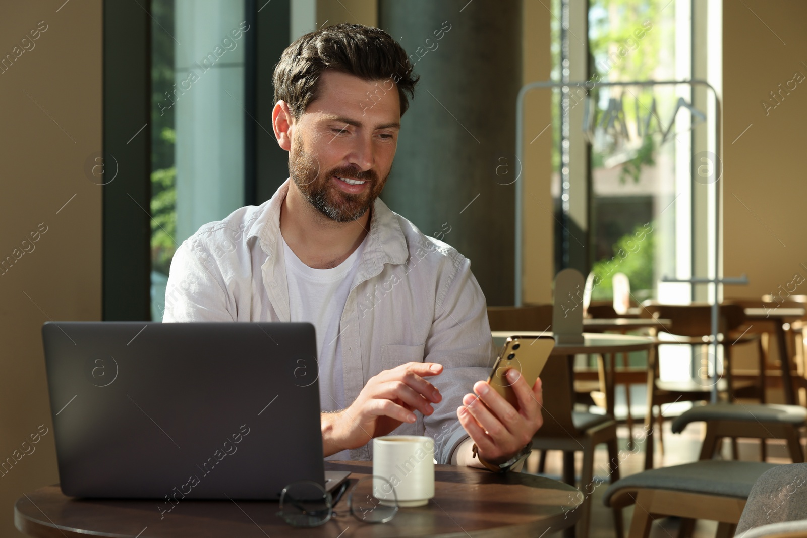 Photo of Man using smartphone and laptop at table in cafe