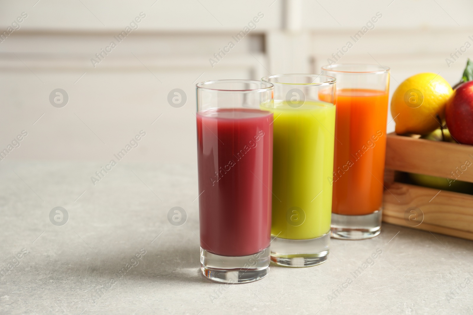 Photo of Three glasses of juices and wooden crate with fresh ingredients on light table. Space for text