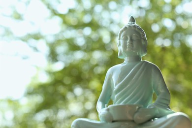 Beautiful ceramic Buddha sculpture on blurred background, closeup. Space for text