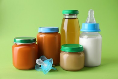 Healthy baby food, juice, milk and pacifier on green background