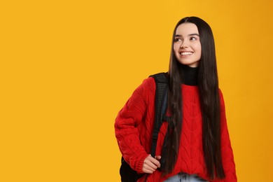 Photo of Happy teenage girl with backpack on yellow background. Space for text