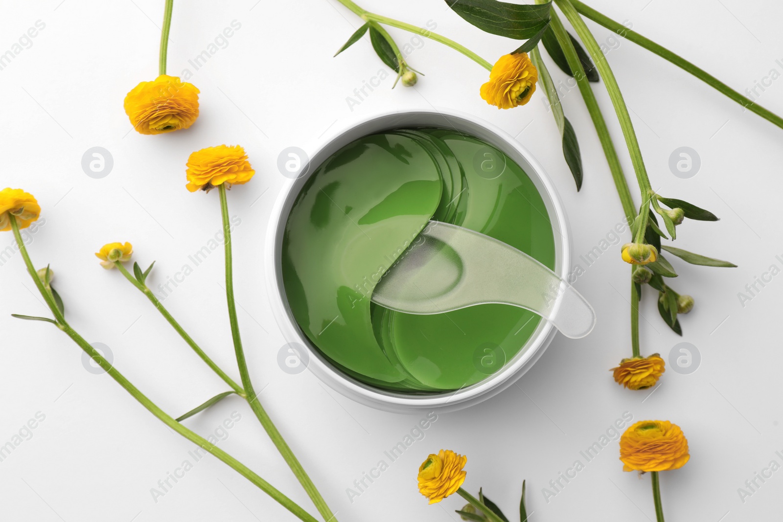 Photo of Jar of under eye patches with spoon and flowers on white background, flat lay. Cosmetic product