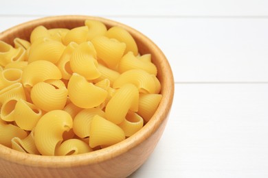 Photo of Raw macaroni pasta in bowl on white wooden table, closeup