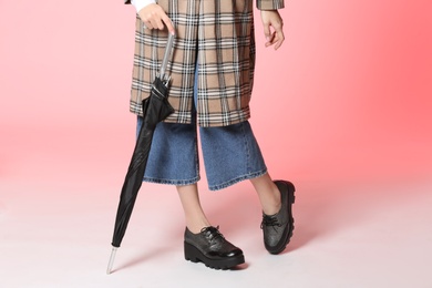 Photo of Woman in stylish shoes and coat holding umbrella on color background