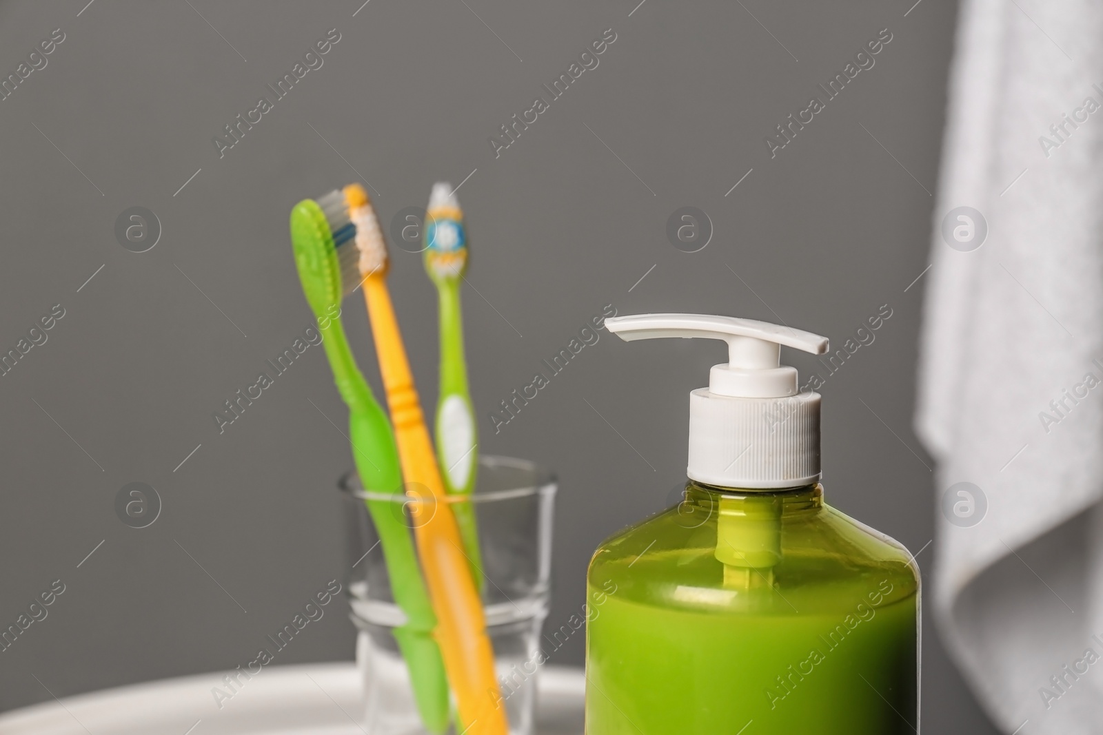 Photo of Glass with toothbrushes and bottle of liquid soap in bathroom