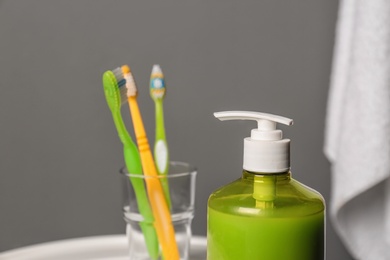 Glass with toothbrushes and bottle of liquid soap in bathroom